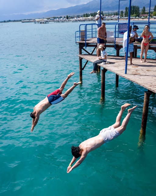 Two travelers diving from a lakeside dock into turquoise water