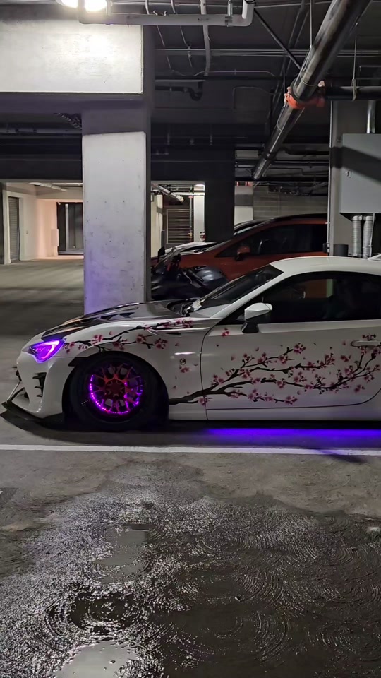 White sports car with cherry blossom livery and purple lighting